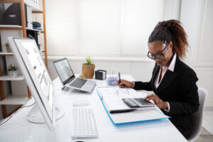 A Black businesswoman typing on a calculator at a desk