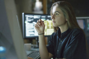Feature image of a young white woman monitoring graphs on a computer