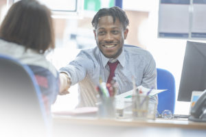 Feature image of a young black businessman shaking hands with a woman across a desk