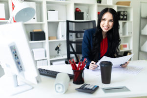 White women with long black hair smiles while sitting in front of a computer at a desk