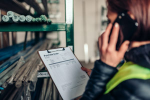 Warehouse clerk using phone and looking at purchase order